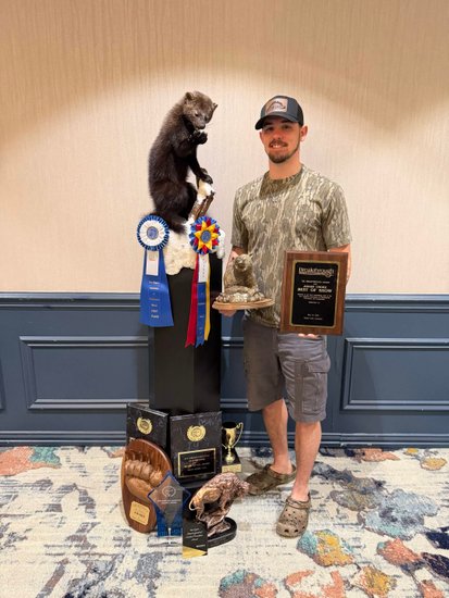 Taxidermist holding a Best of Show plaque beside a fisher mount